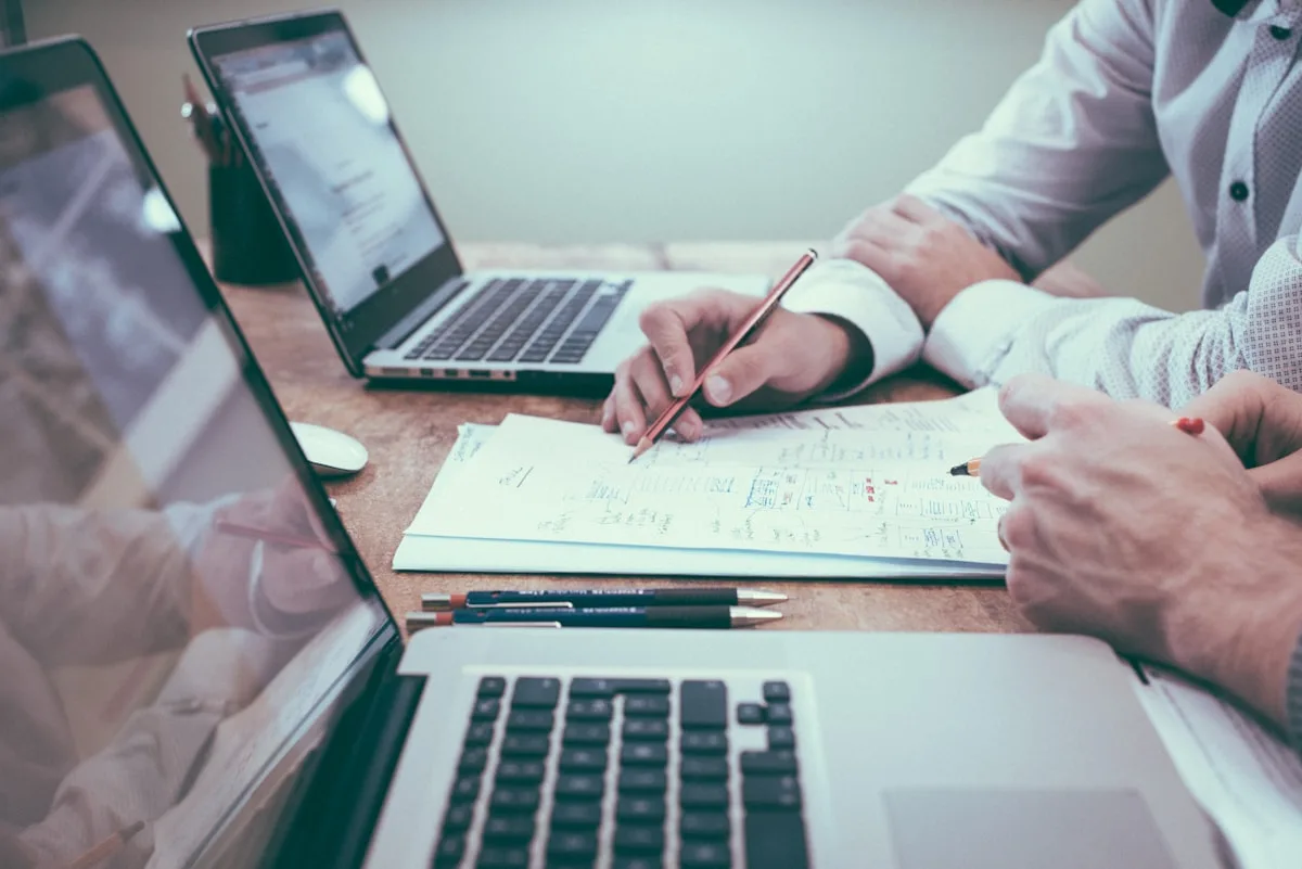 Equipe conferindo documentos e dados lado a lado com notebooks